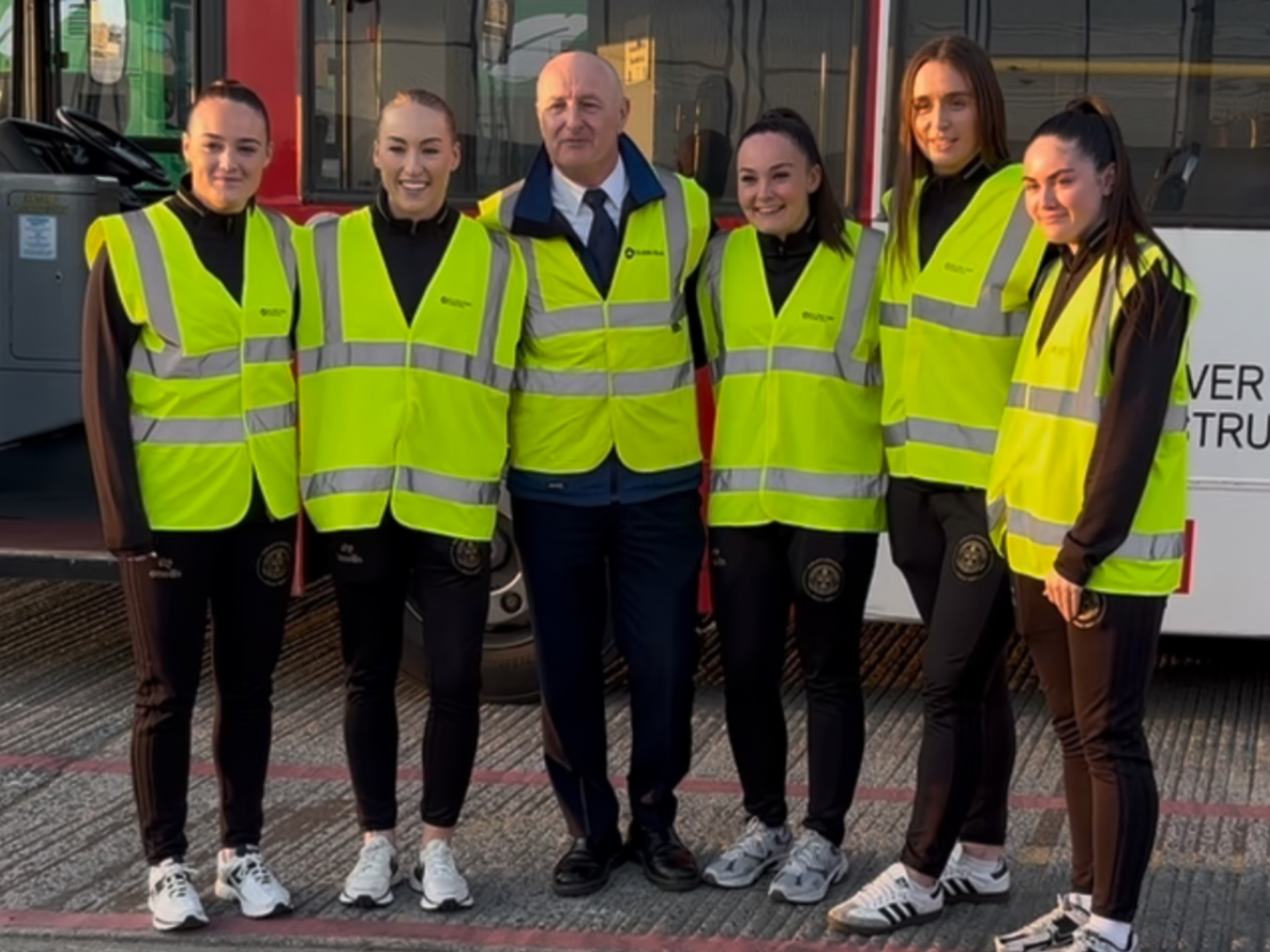 Image of 5 Female Bohs Players standing in front of a red learner bus with a Dublin Bus driving instructor.