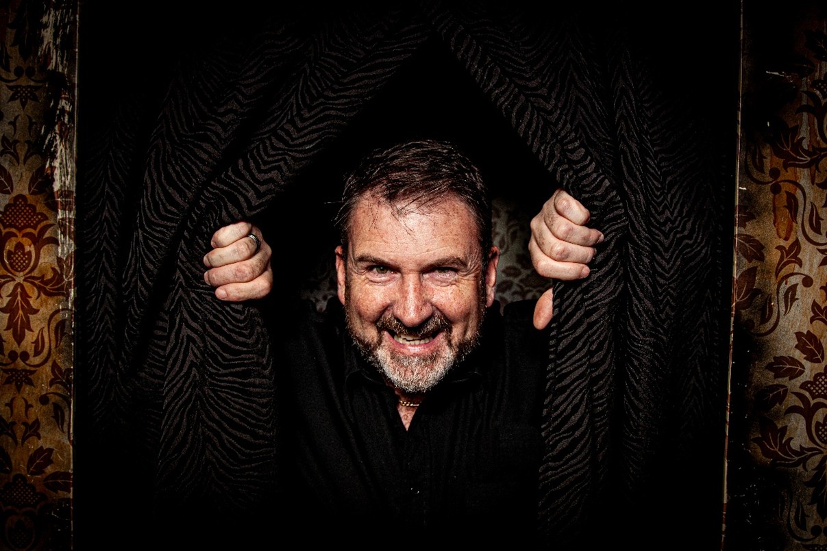Image of a a man peaking his head out of curtains in a dark room